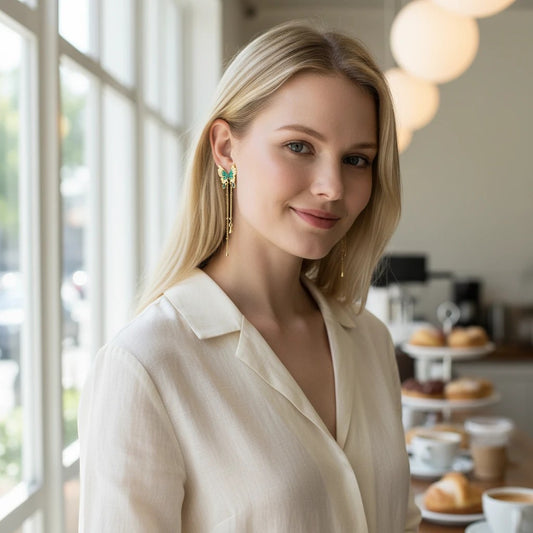 TITLIYA blue butterfly drop earrings with gold chains worn by a blonde woman in a cafe setting.