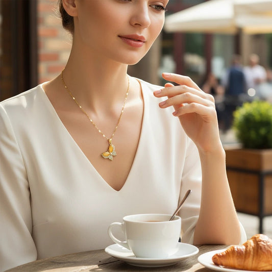 Woman wearing a TITLIYA gold-toned butterfly pendant necklace with crystal accents at an outdoor cafe.