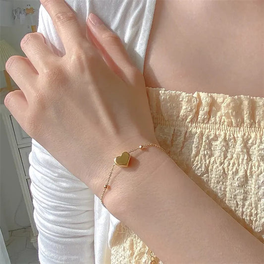TITLIYA delicate gold heart charm bracelet with dainty bead accents on a fine chain worn on a woman's wrist.