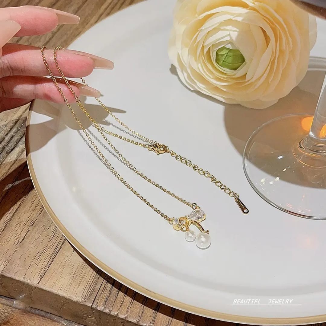 TITLIYA gold plated necklace featuring a delicate bow pendant with sparkling crystals and two small white pearls.