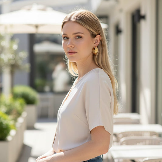 Woman wearing elegant TITLIYA golden twisted hoop earrings in a bright outdoor cafe setting.