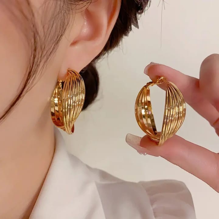 TITLIYA golden twisted hoop earrings worn on ear and held by hand, featuring a multi-layered elegant design.