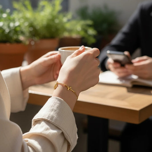 TITLIYA gold-tone heartbeat and heart charm bracelet worn on a woman's wrist while holding a coffee cup outdoors.