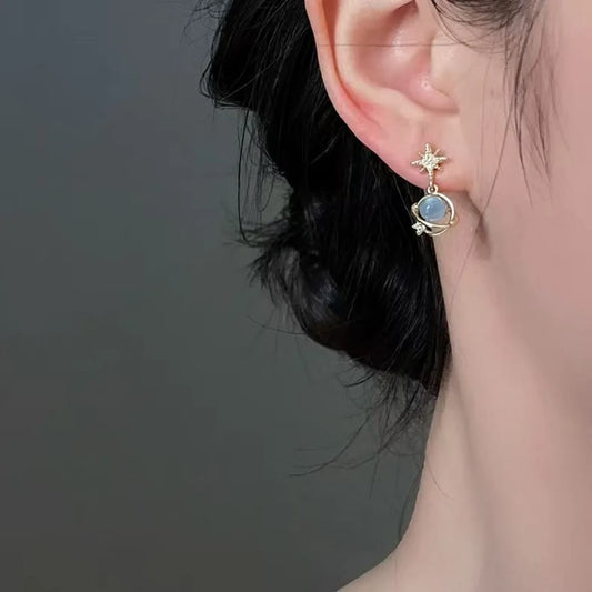TITLIYA gold-tone Saturn design earring with a blue stone and star accent worn on a woman's ear.