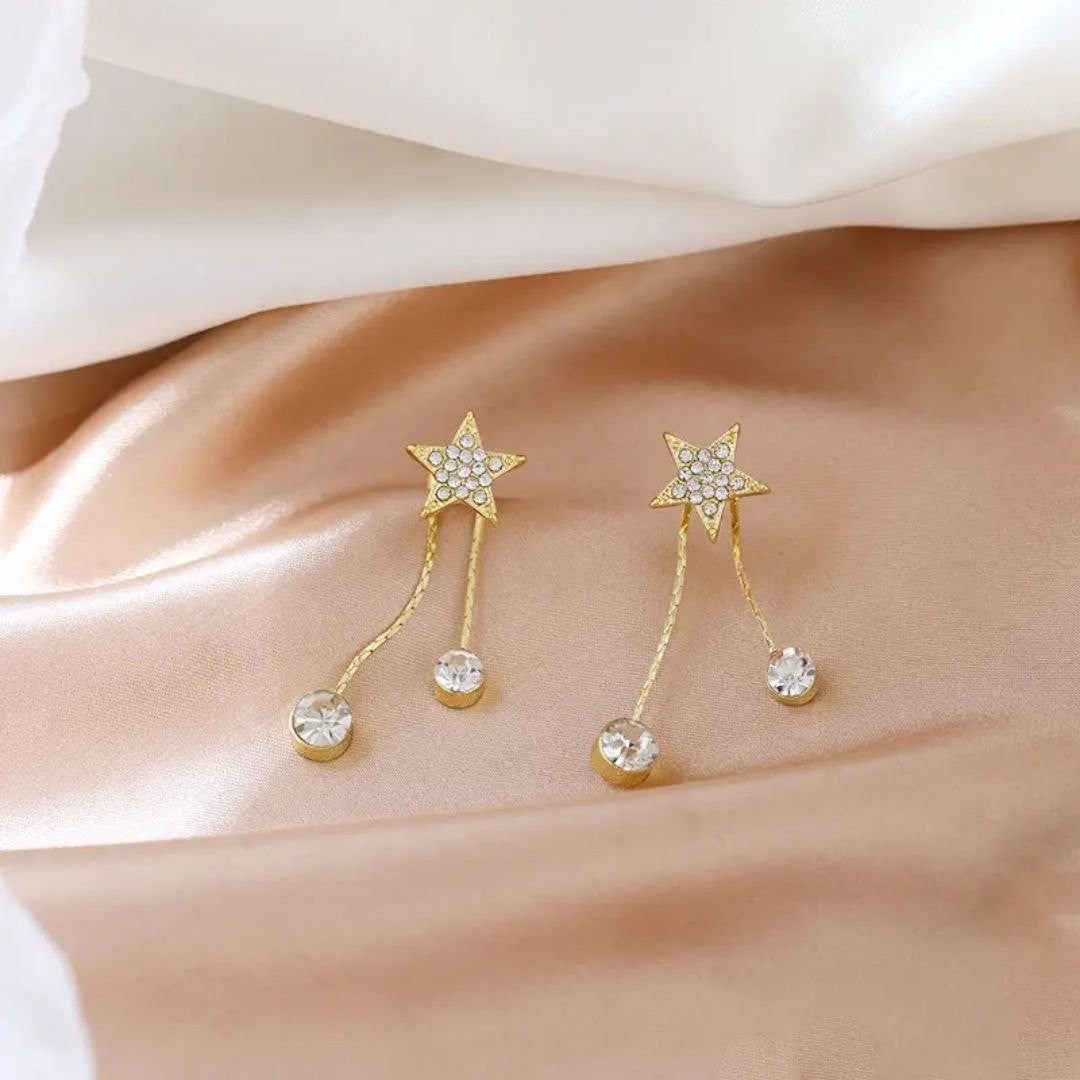 TITLIYA gold-tone star drop earrings featuring sparkling crystal accents on a soft satin background.
