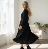 Model wearing large black flower earrings by TITLIYA, styled with a black dress in a bright, modern living room.