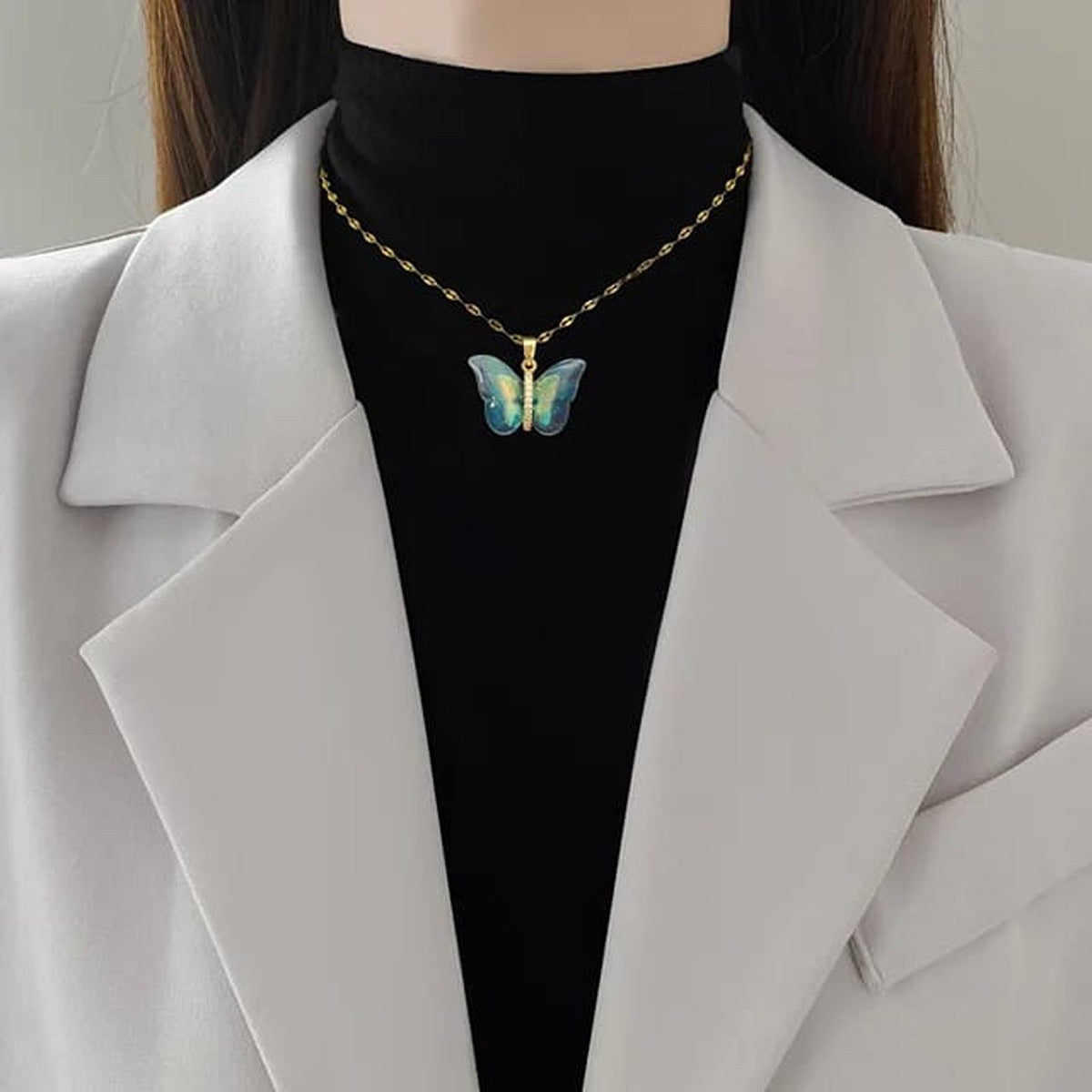 TITLIYA blue butterfly pendant necklace on a gold chain worn over a black turtleneck and white blazer