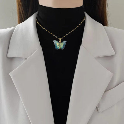 TITLIYA blue butterfly pendant necklace on a gold chain worn over a black turtleneck and white blazer