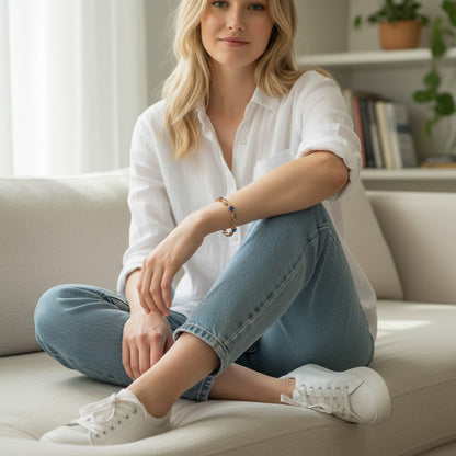 Woman wearing a TITLIYA blue tulip bracelet with gold accents, styled with a white shirt and jeans on a sofa.