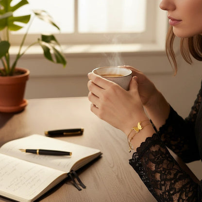 TITLIYA gold-tone butterfly charm bracelet with beaded chain worn by a woman holding a steaming cup at a desk.