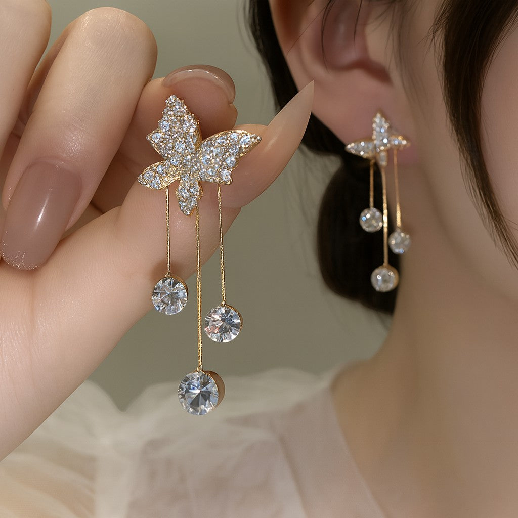 TITLIYA gold-tone butterfly dangle earrings with sparkling crystal accents, worn by a woman for a festive look.
