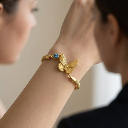 TITLIYA gold-tone butterfly charm bracelet with a blue evil eye bead on a model's wrist, boho style accessory.