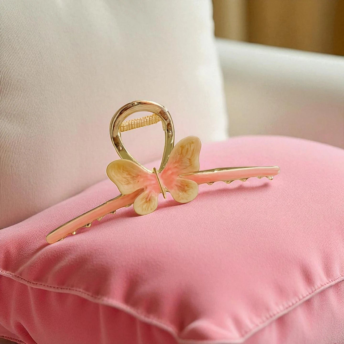 TITLIYA butterfly hair claw in pink and cream enamel with a gold finish, resting on a soft pink cushion.