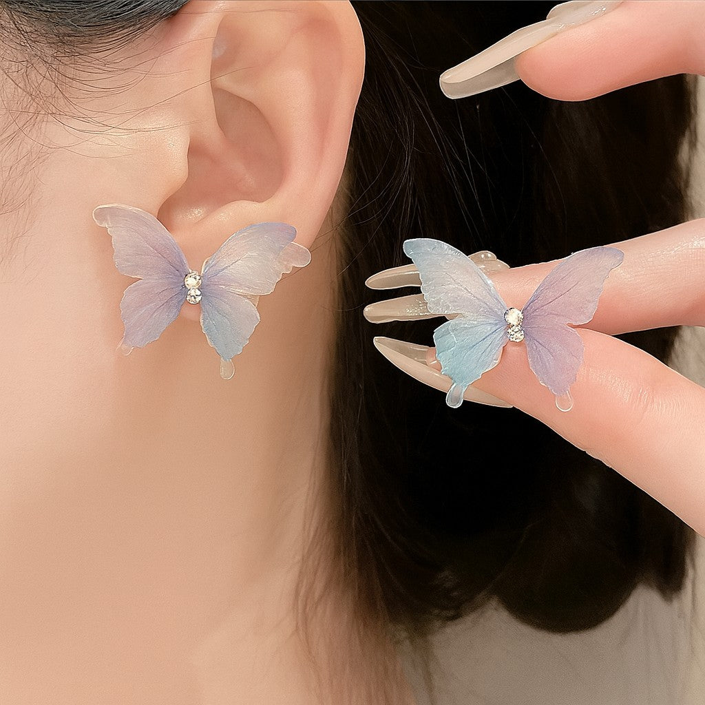 TITLIYA feather-light butterfly stud earrings in pastel blue and purple with a central crystal accent on a model.