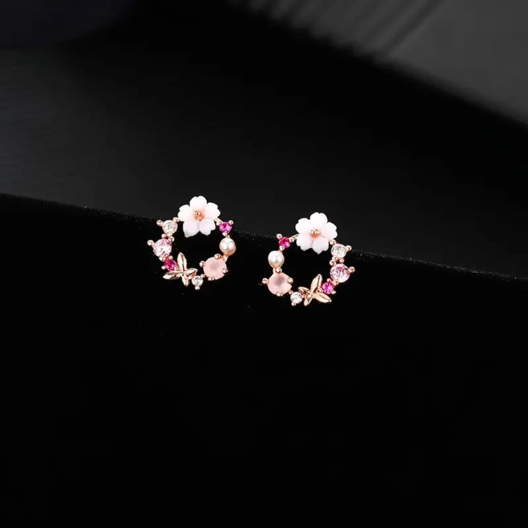TITLIYA mini flower and butterfly stud earrings with pink crystals and white floral accents on a black background.
