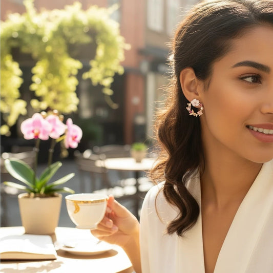 Woman wearing TITLIYA mini flower and butterfly earrings with pink and white floral accents at an outdoor cafe.