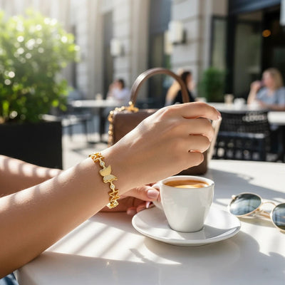 TITLIYA gold bracelet with multiple butterfly charms and delicate stone accents worn at an outdoor cafe table.