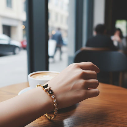 TITLIYA gold plated butterfly and flower bracelet with sparkling crystals worn on a wrist at a cafe table.