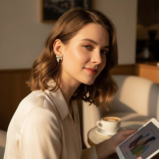 Woman wearing TITLIYA gold-plated butterfly stud earrings, styled with a cream blouse in a warm cafe setting.