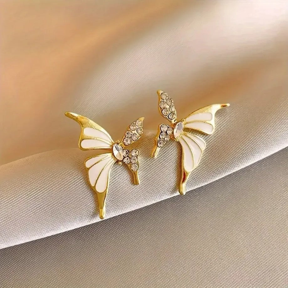 TITLIYA gold-plated butterfly stud earrings with white enamel and sparkling crystal accents on a silk background.