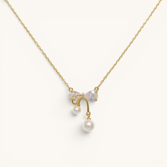 TITLIYA gold-plated necklace featuring a crystal bow pendant with two dangling white pearls on a delicate chain.