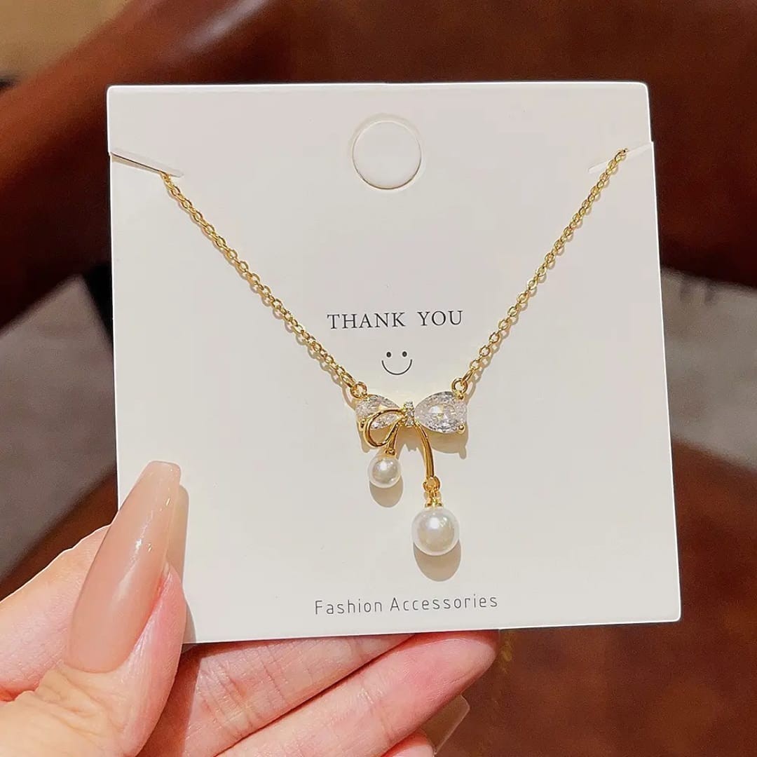 TITLIYA gold plated necklace featuring a crystal bow pendant with two dangling white pearls on a display card