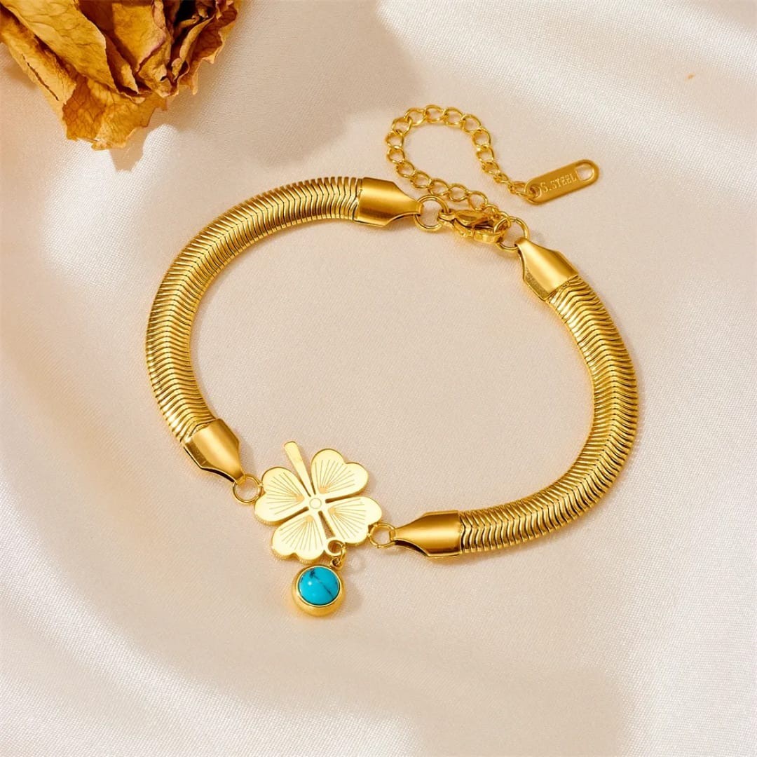 TITLIYA gold-tone snake chain bracelet with a heart-leaf clover charm and a blue evil eye pendant on satin fabric.