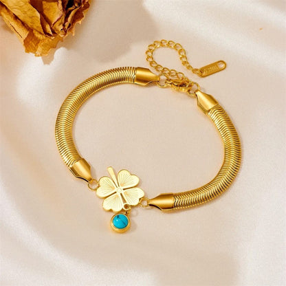 TITLIYA gold-tone snake chain bracelet with a heart-leaf clover charm and a blue evil eye pendant on satin fabric.