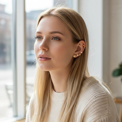 Woman wearing a TITLIYA set of 12 gold stud earrings featuring heart, pearl, and geometric designs.