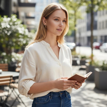 Woman wearing TITLIYA gold stud earrings while reading a book outdoors in a casual white shirt and jeans.