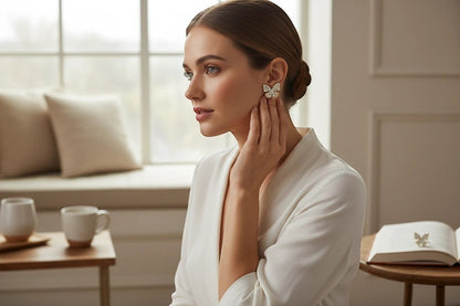 Woman wearing TITLIYA golden butterfly stud earrings with diamond dust finish in a bright, elegant indoor setting.