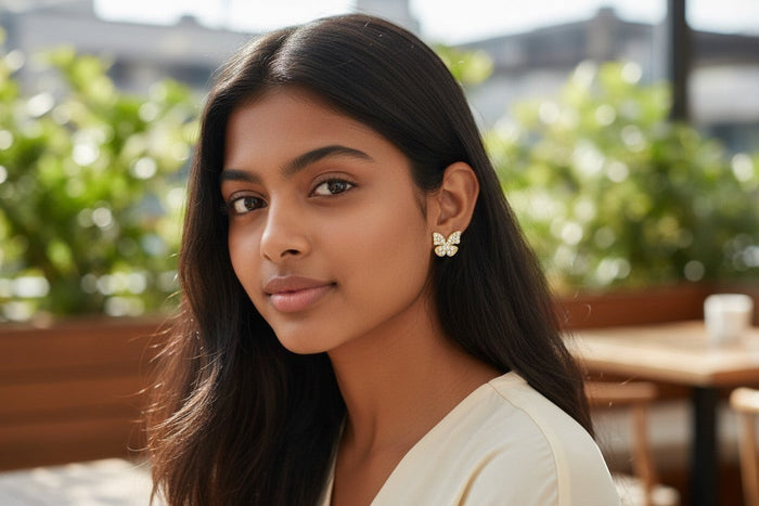 A model wearing TITLIYA golden butterfly stud earrings with a sparkling diamond dust finish in an outdoor setting.