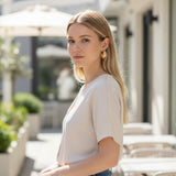 Woman wearing elegant TITLIYA golden twisted hoop earrings in a bright outdoor cafe setting.