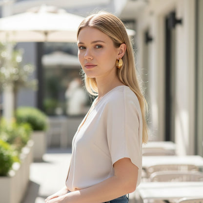 Woman wearing elegant TITLIYA golden twisted hoop earrings in a bright outdoor cafe setting.