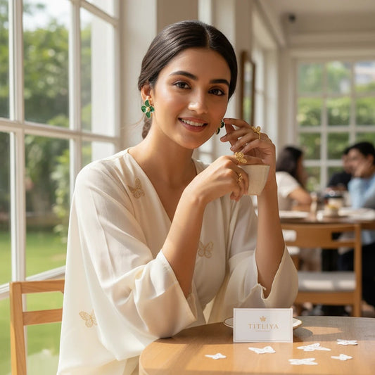 Woman wearing elegant green flower earrings by TITLIYA, styled with a white dress in a bright cafe setting.