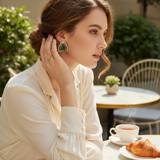Woman wearing elegant TITLIYA gold-tone earring with a green stone, styled for everyday wear at a cafe.
