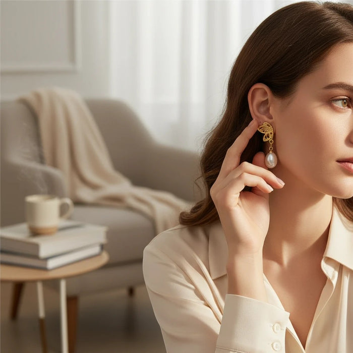 TITLIYA gold half butterfly stud earrings with hanging pearl, worn by a woman in a chic, elegant setting.