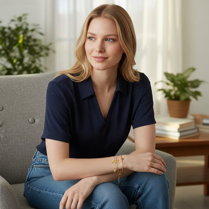 Woman wearing a TITLIYA gold-toned layered butterfly charm bracelet with white inlay, styled with a navy polo shirt.