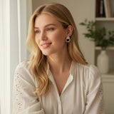 Woman wearing TITLIYA peach round crystal flower earrings with a white blouse in a bright indoor setting.
