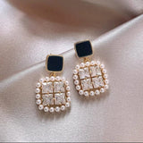 TITLIYA premium square earrings featuring black studs, clear crystals, and a pearl border on a silk background.