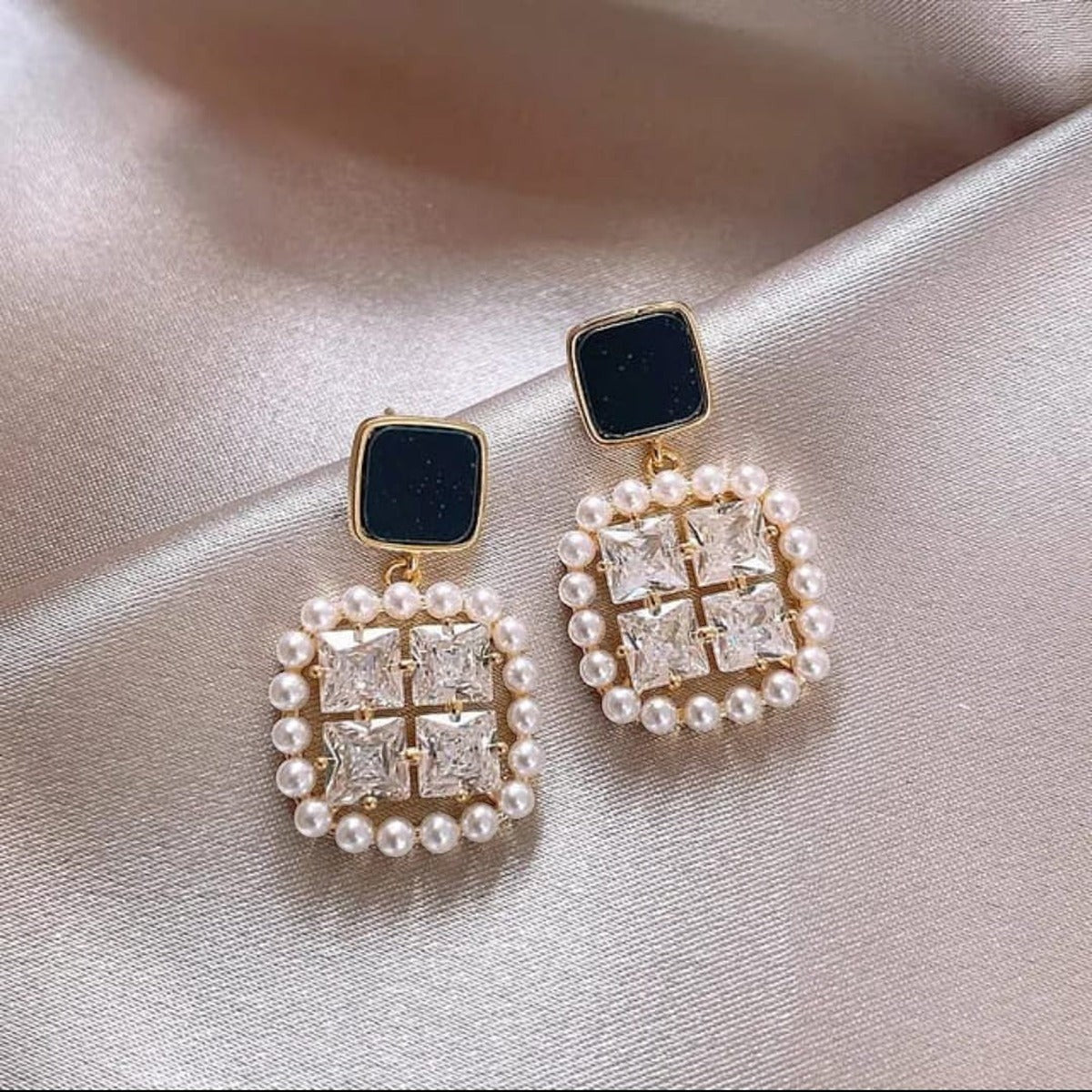 TITLIYA premium square earrings featuring black studs, clear crystals, and a pearl border on a silk background.