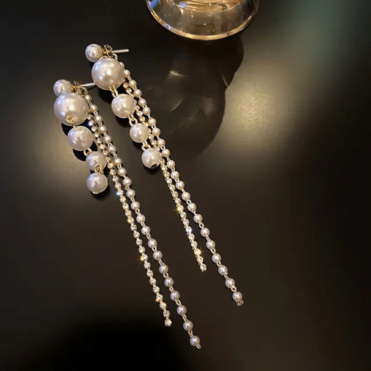 TITLIYA elegant Korean-style long drop earrings featuring white pearls and delicate crystal chains on a black surface.