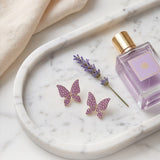 TITLIYA pink butterfly stud earrings with crystal embellishments on a marble tray with lavender and perfume.
