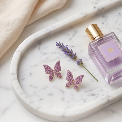 TITLIYA pink butterfly stud earrings with crystal embellishments on a marble tray with lavender and perfume.