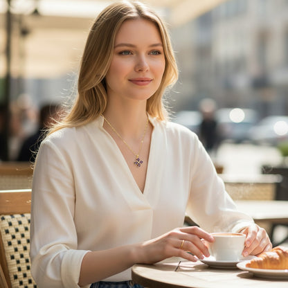 Woman wearing a TITLIYA gold flower pendant necklace with purple stones at an outdoor cafe.