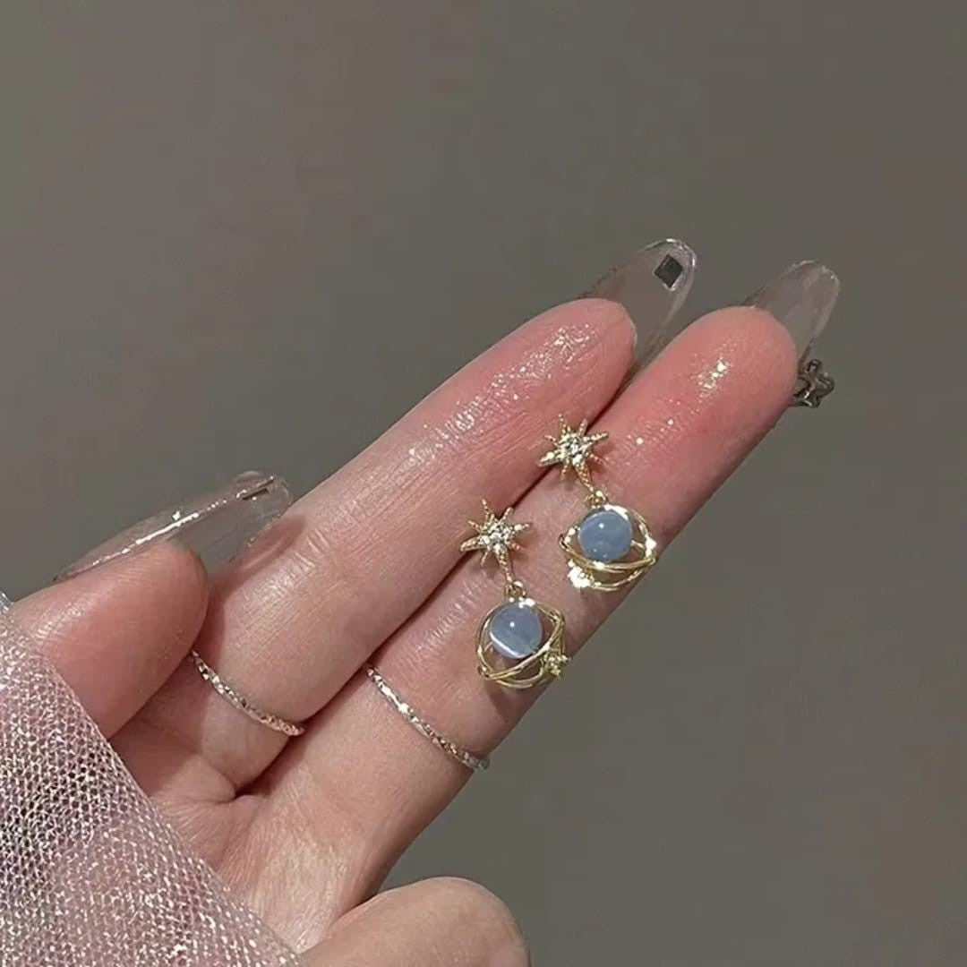 TITLIYA gold-tone Saturn design earrings featuring blue spherical stones and star accents on a hand.