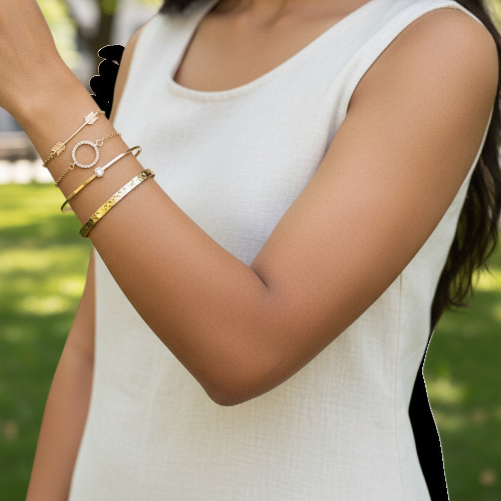 Woman wearing a TITLIYA set of four gold-toned bracelets with delicate charms and minimalist designs outdoors.