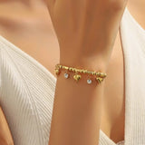 TITLIYA gold-tone bracelet with heart charms and clear stone accents on a model wearing a white ribbed top.