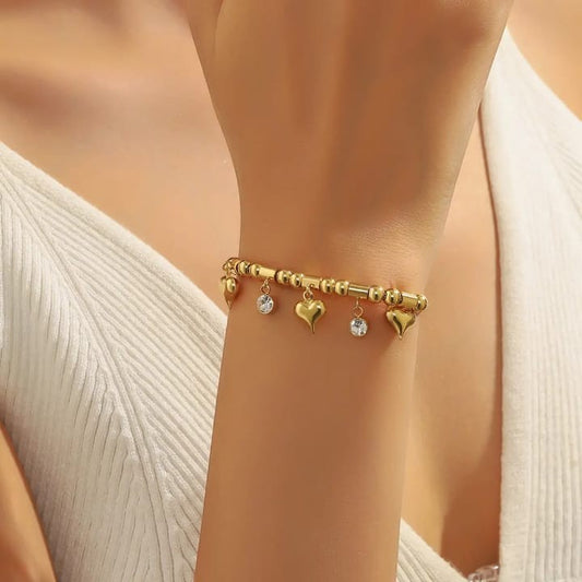 TITLIYA gold-tone bracelet with heart charms and clear stone accents on a model wearing a white ribbed top.