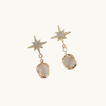 TITLIYA gold-tone star drop earrings featuring sparkling crystals and a dangling white pearl-like stone for elegance.